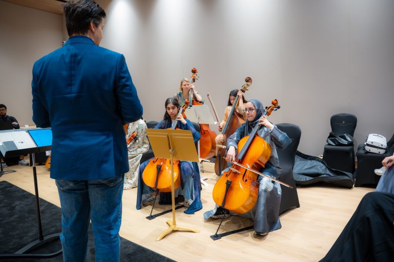 Cellists rehearsing with a conductor in the Empowering Emirati Musicians Program